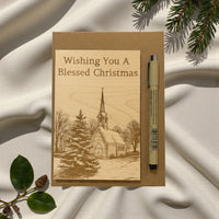 Card with 'Wishing You A Blessed Christmas' text and a pen on a textured fabric background.