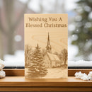 Wooden Christmas card with a church illustration and 'Wishing You A Blessed Christmas' text, set against a snowy landscape.