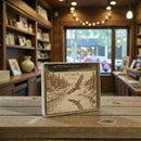 Decorative box with engraved design of eagles and nature scene on a wooden table.