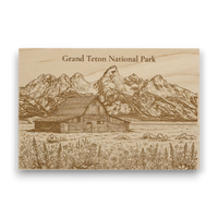 Wooden plaque with engraved illustration of a barn and mountains labeled 'Grand Teton National Park'.