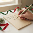 Hand writing a message on a wooden board with Christmas decorations in the background