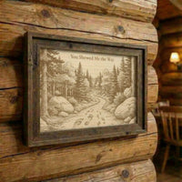 Framed artwork of a forest scene with a path on a wooden wall.