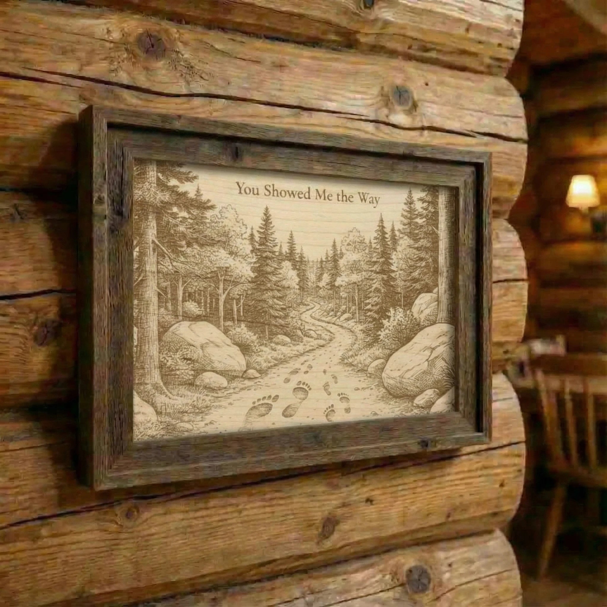 Framed artwork of a forest scene with a path on a wooden wall.