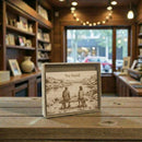 Engraved card with a scenic illustration of two people on a bench in a store setting.