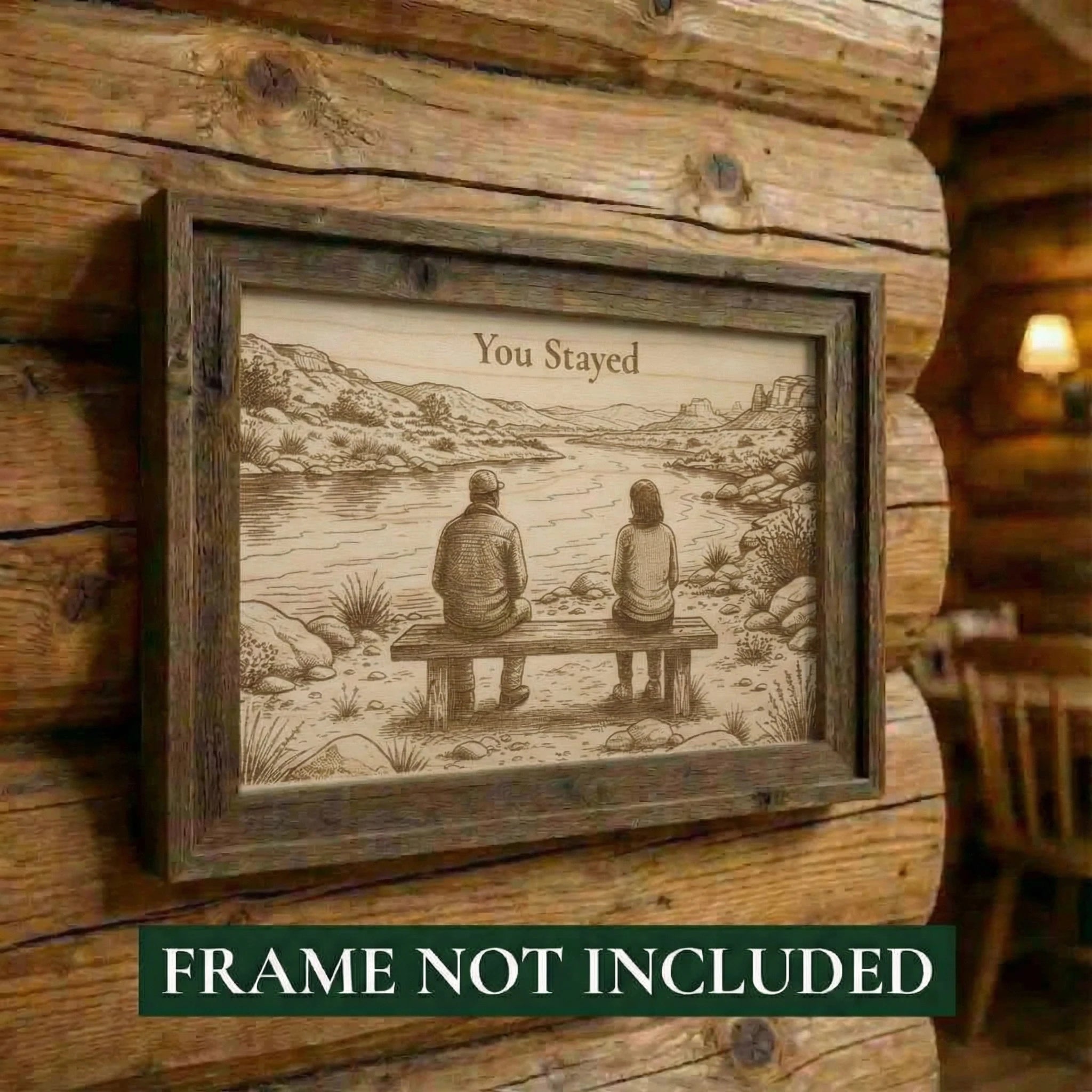 Framed artwork of a couple sitting on a bench by a lake, with text 'You Stayed', on a wooden wall.
